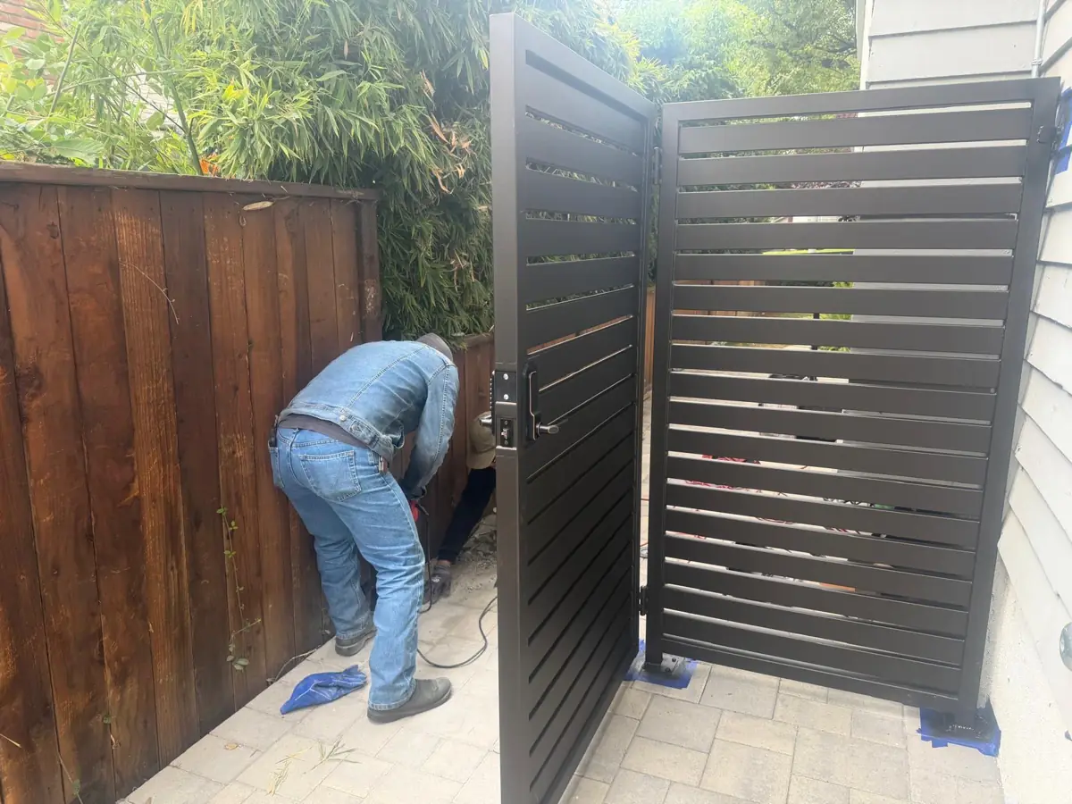 Technician fitting a black slat gate beside a wood fence