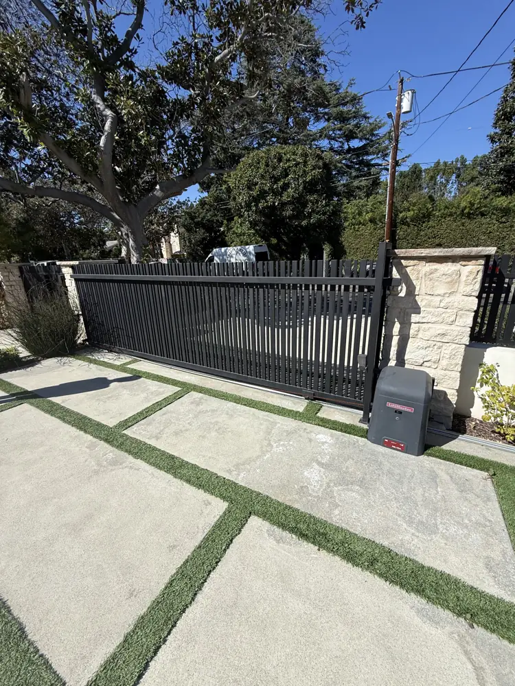 Black sliding driveway gate between stone pillars