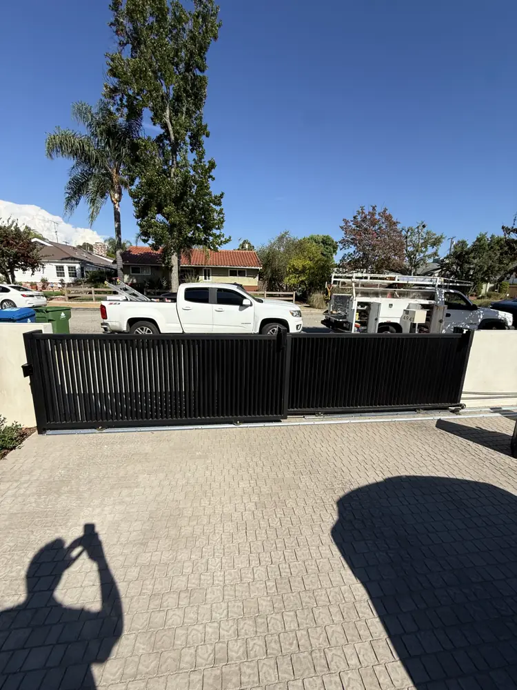 Black slat driveway gate across a paver driveway