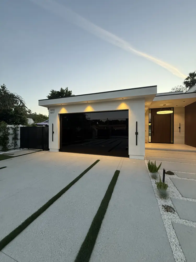 Modern frameless black glass garage door lit at dusk