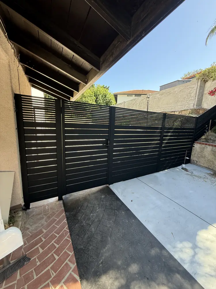Black horizontal fence above a brick driveway