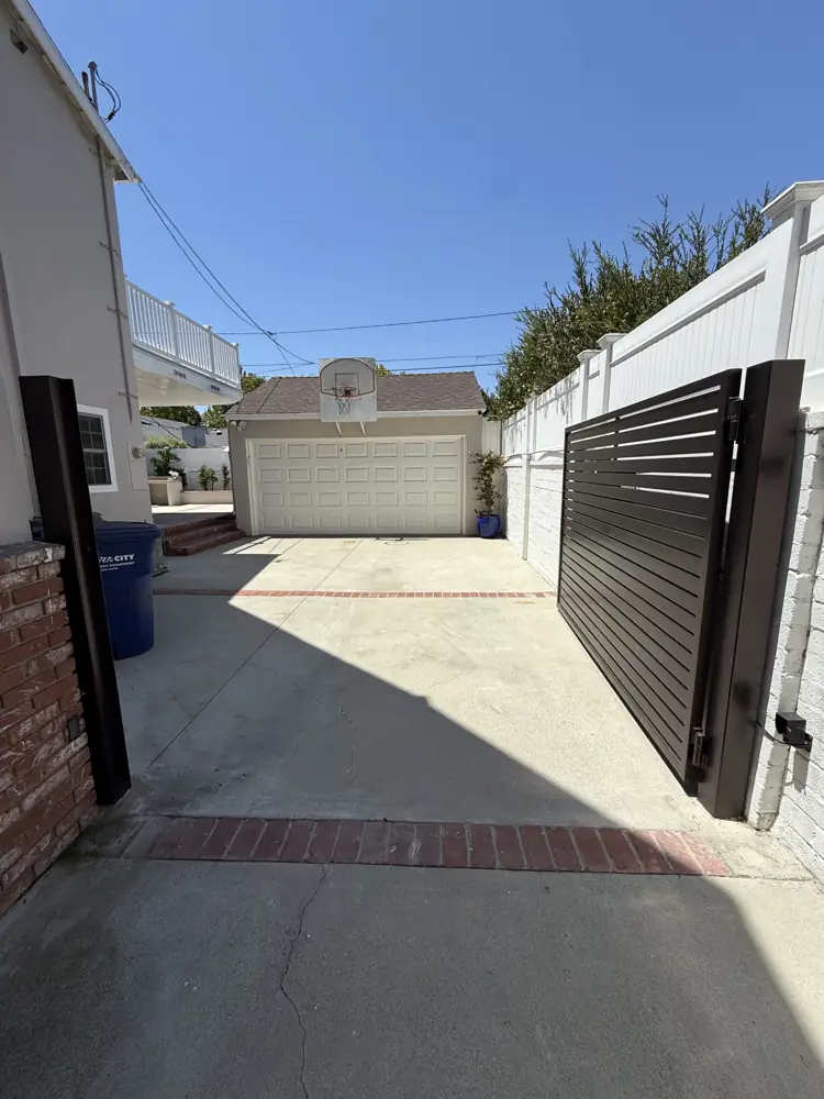 Black slat driveway gate open to a long driveway