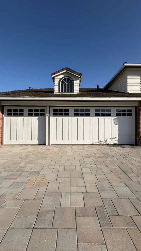 Three white carriage-house garage doors over a paver driveway