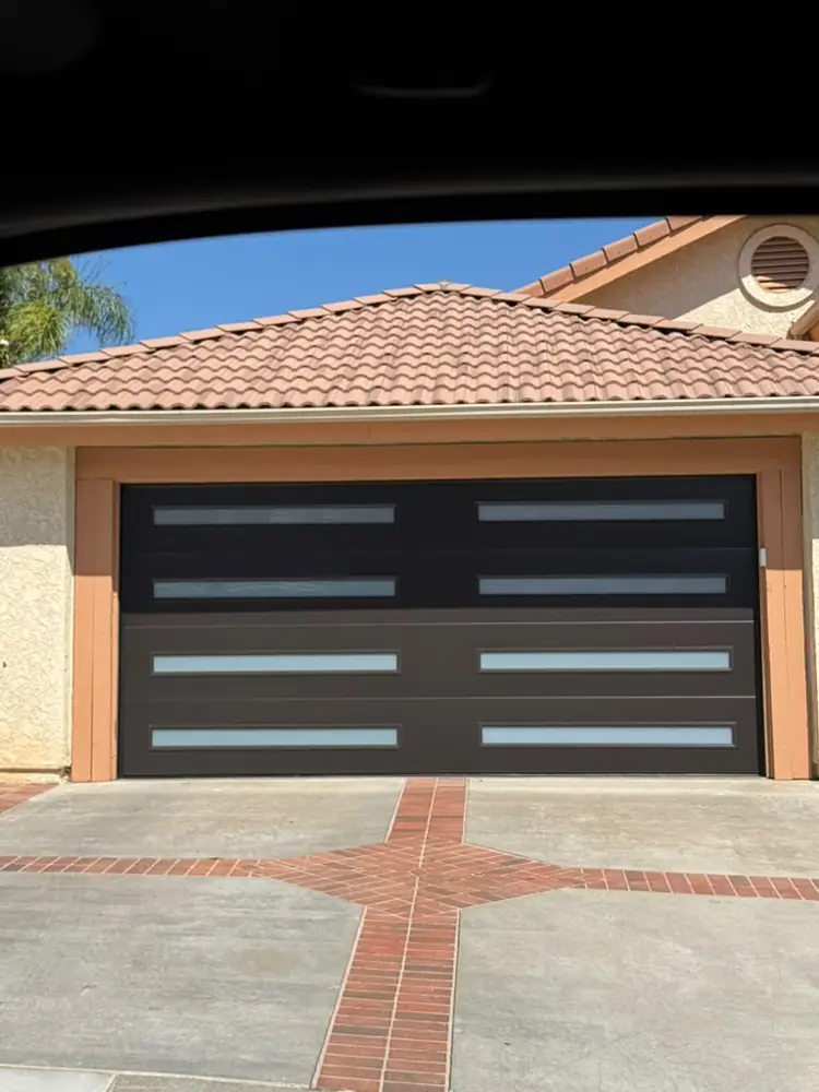 Black modern garage door with frosted windows under a tile roof